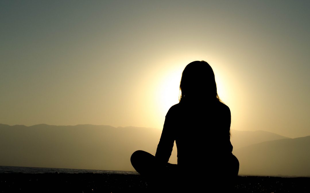 Person sitting on a mountain top at sunrise in meditation